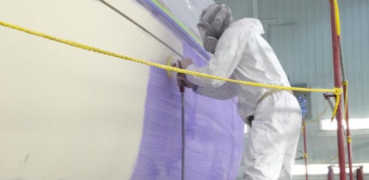 Worker preparing a boat hull for paint